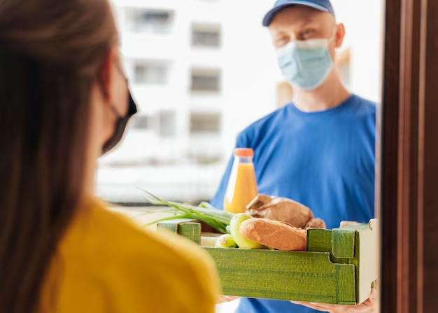 Доставка продуктів додому під час хвороби — кур’єр передає коробку з їжею Доставка продуктів додому під час хвороби — кур’єр передає коробку з їжею